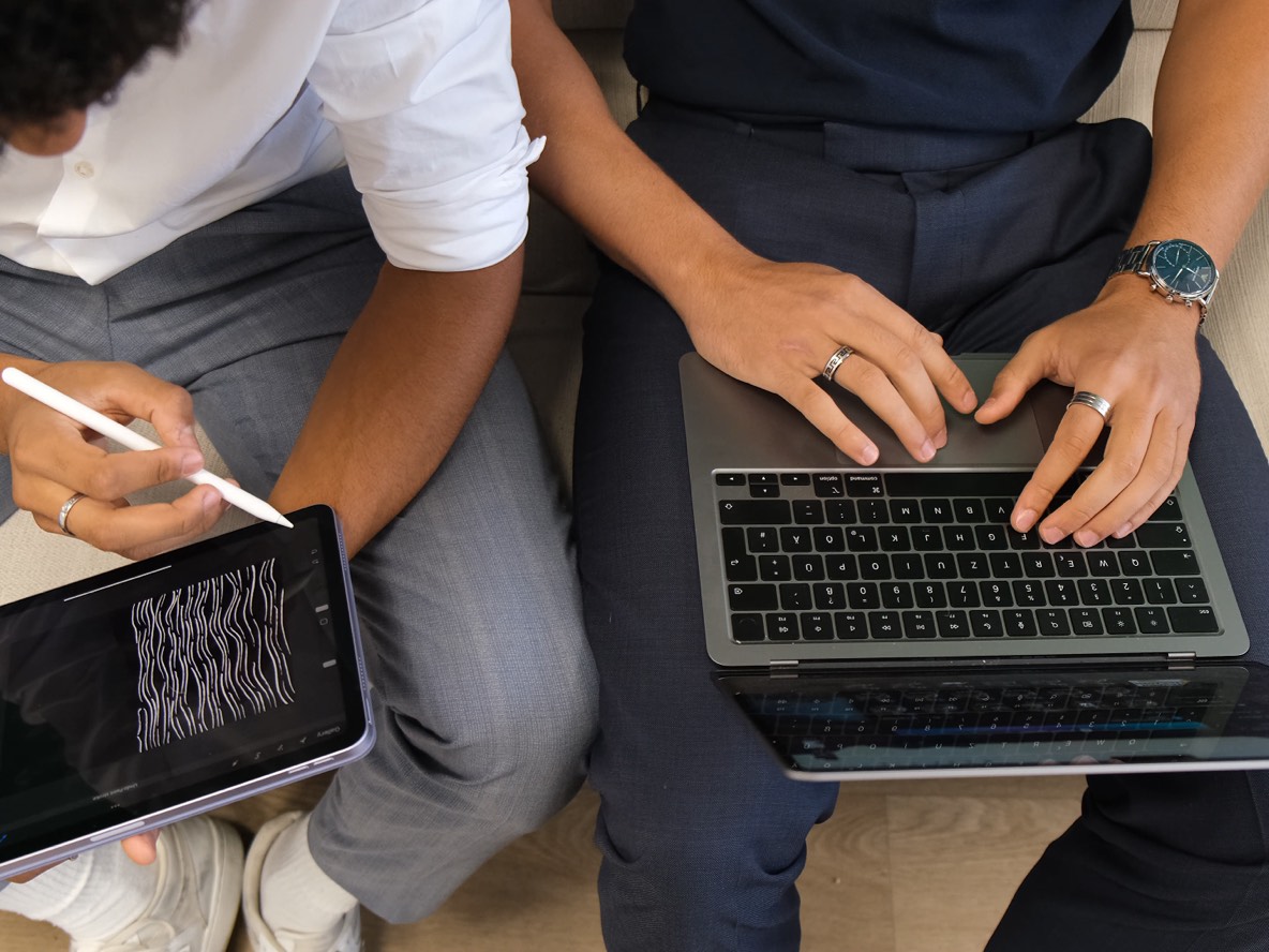 Zwei Personen arbeiten nebeneinander an Tablet und Laptop