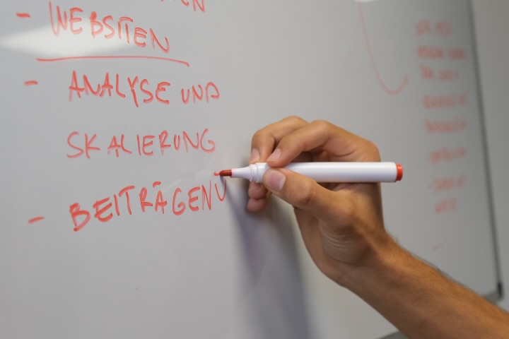 Hand schreibt Stichworte zu Websites, Analyse und Skalierung an ein Whiteboard